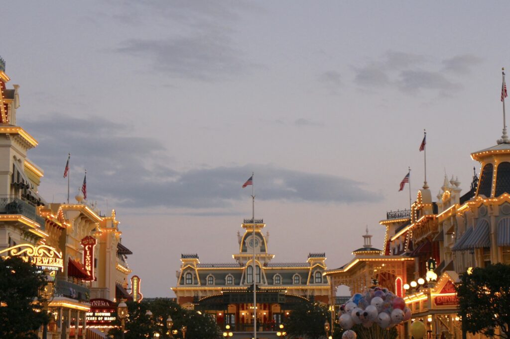 A pastel sky sits behind the white light lined train station and buildings that frame it on Main Street at Magic Kingdom