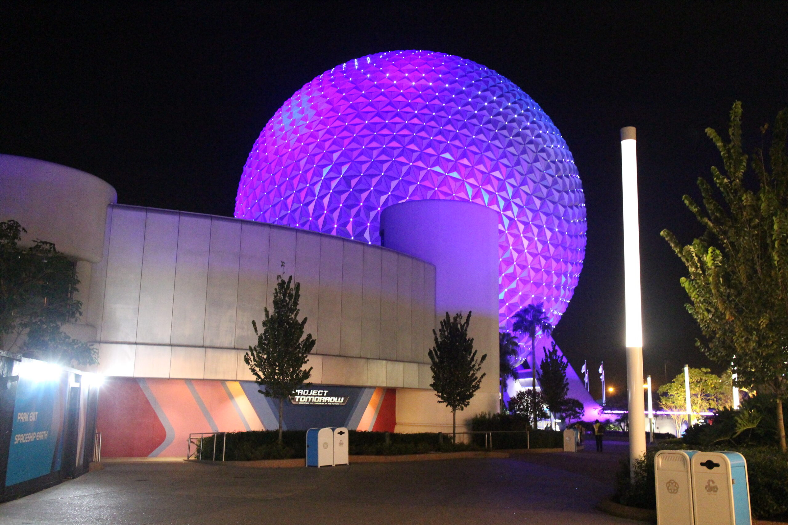 a geodesic sphere known as Spaceship Earth is lit in blue and purple behind the corresponding ride buidling