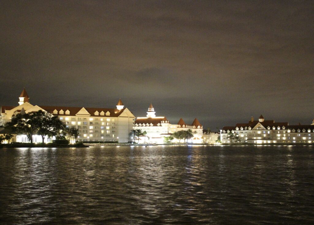 The Grand Floridian resort at Walt Disney World glows white in front of a night sky and over the dark Seven Seas Lagoon.