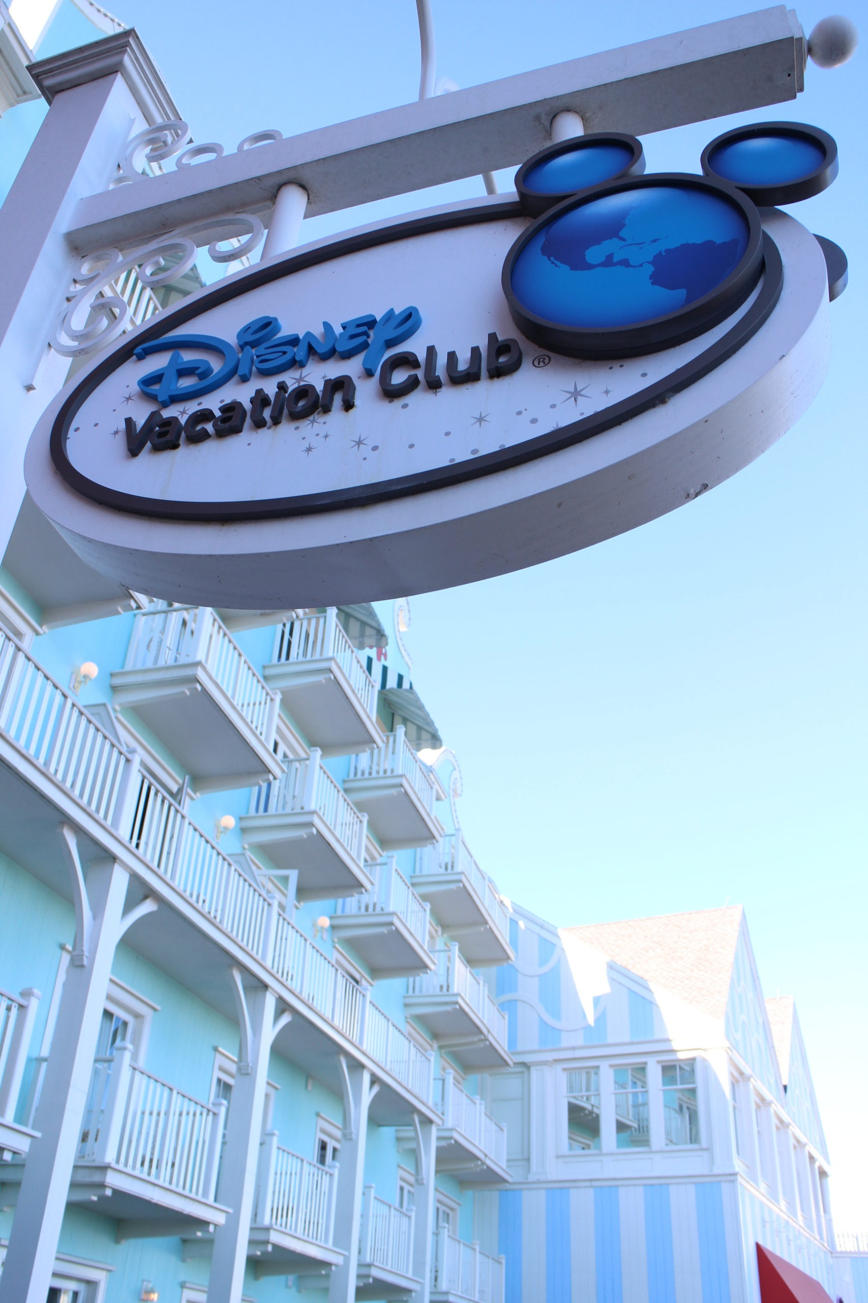 Disney Vacation Club sign with logo hangs in front of bright mint hotel building with balconies