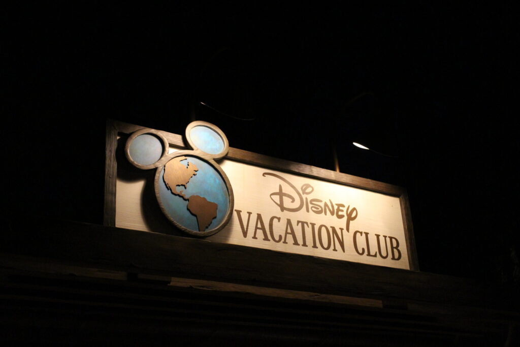 Nighttime with a lit Disney Vacation Club sign with the earth logo that has Mickey ears