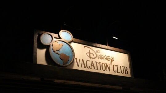Nighttime with a lit Disney Vacation Club sign with the earth logo that has Mickey ears