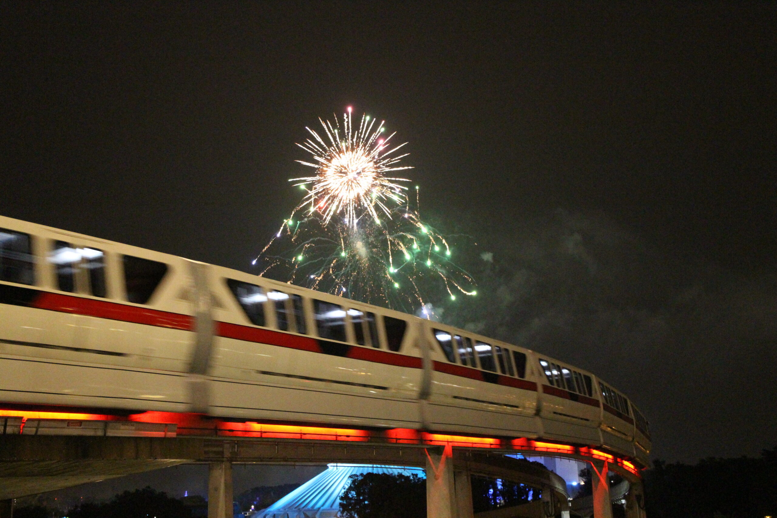 Monorail whizzing by a dark sky with Magic Kingdom fireworks overhead
