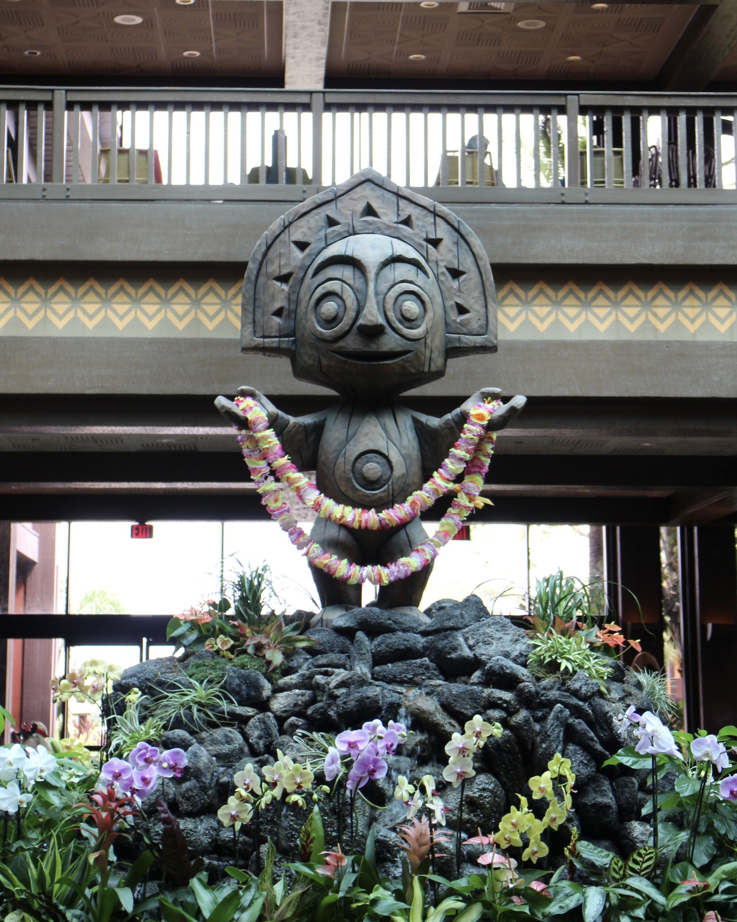 A tiki statue holds up a lei on top of a rock surrounded by flowers in Disney's Polynesian Village Resort lobby