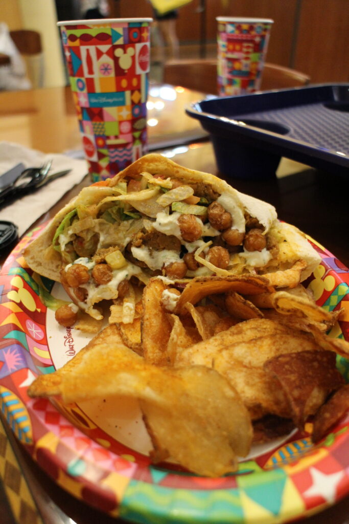 A gyro in a pita next to house made chips on a colorful Disney World paper plate