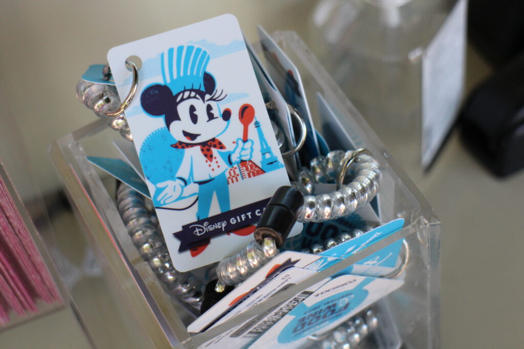 An white Epcot Food and Wine Disney gift card with a bracelet attached with Chef Minnie on it