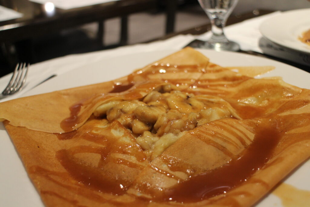 A closeup of a golden brown banana crepe, drizzled with caramel on a white crepe