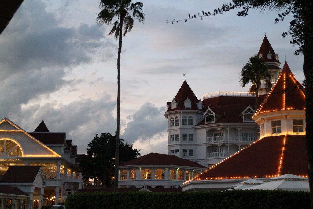 Grand Floridian sunset with puffy clouds and light blue skies over the white buildings and red roofs with white lights