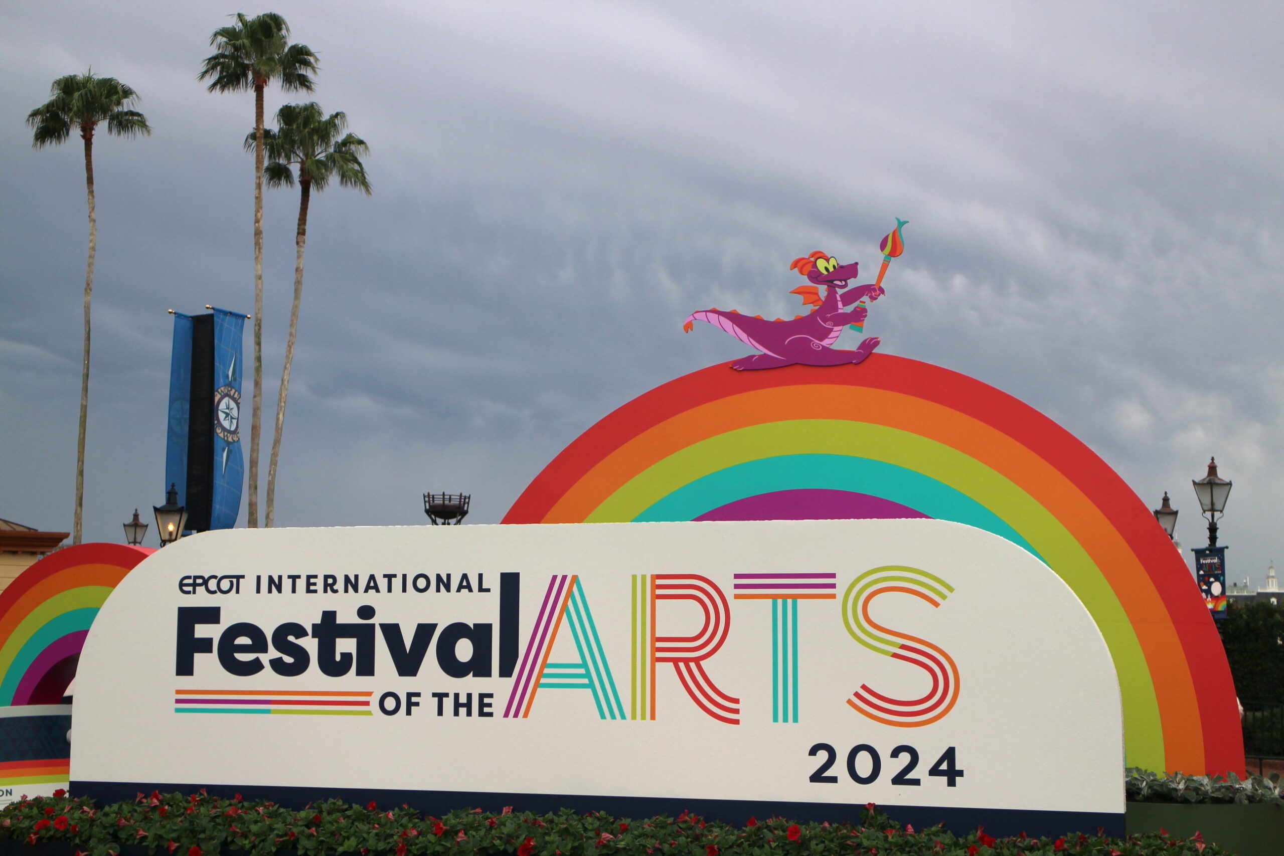 a rainbow with a small purple dragon on it over an Epcot Festival of the Arts sign
