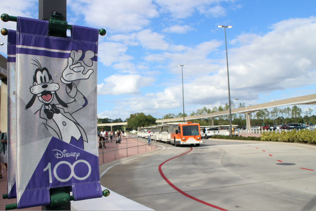 a Disney 100 sign and tram in the Epcot parking lot