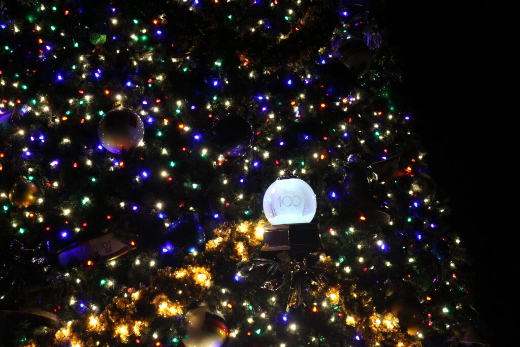 a Disney 100 ornament glows in between lights on a dark Christmas tree