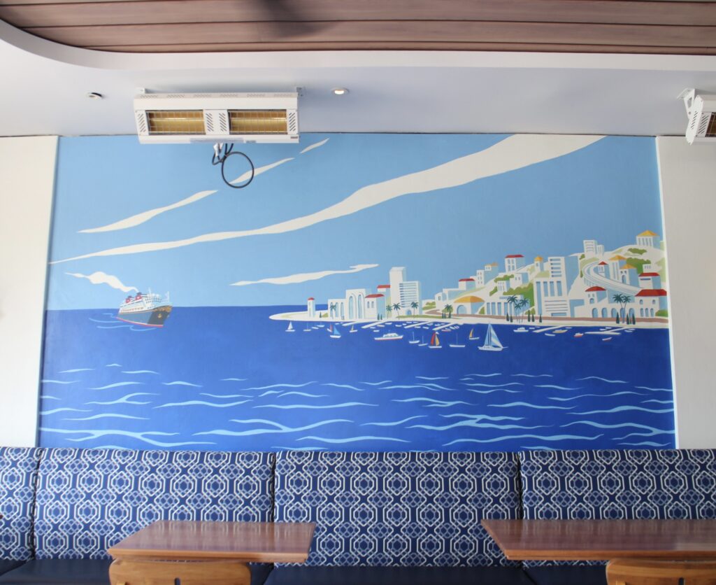 Booth seating in front of a blue mediterranean style art mural at Bar Riva at Riviera resort