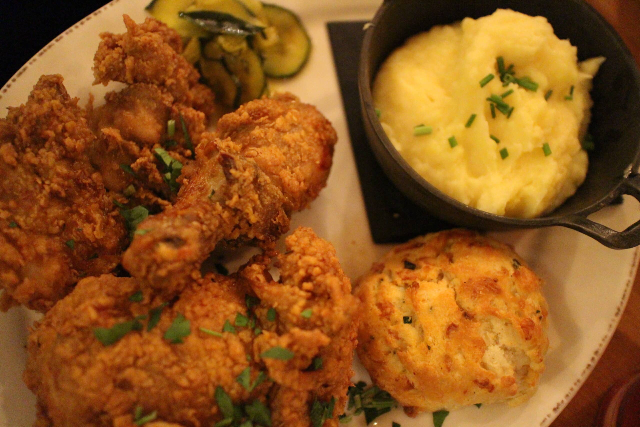Fried chicken, mashed potatoes, a biscuit and pickles on a white plate at Homecomin'