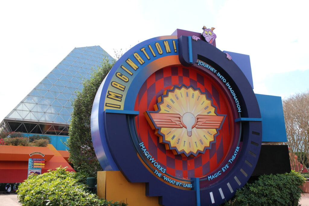 a circular, colorful sign in front of the glass pyramid Imagination Pavilion at Epcot which has the DVC lounge inside
