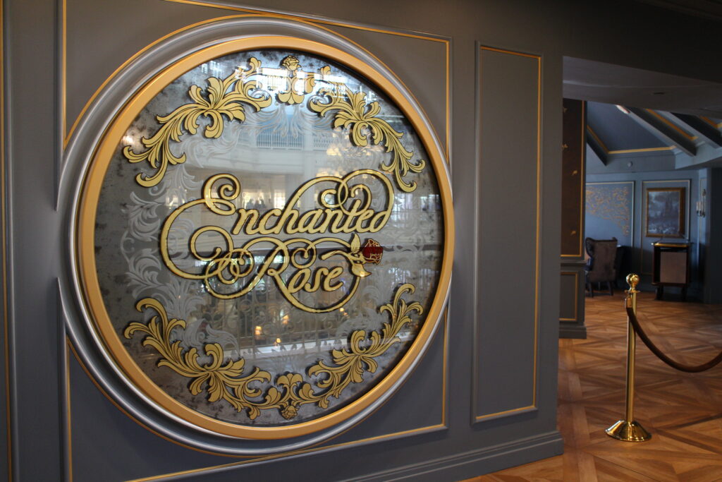a gilded round mirror that says Enchanted Rose in a fancy script on a dark wall in front of a bar and lounge venue