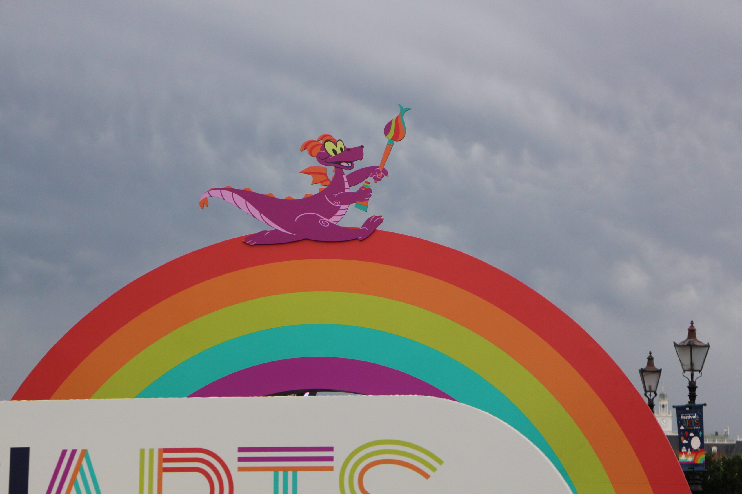 a little purple dragon sits on a rainbow sign