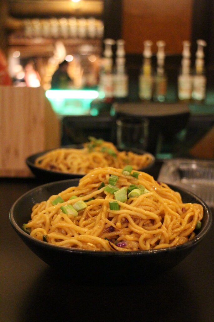 A bowl of noodles topped with chives on a bar