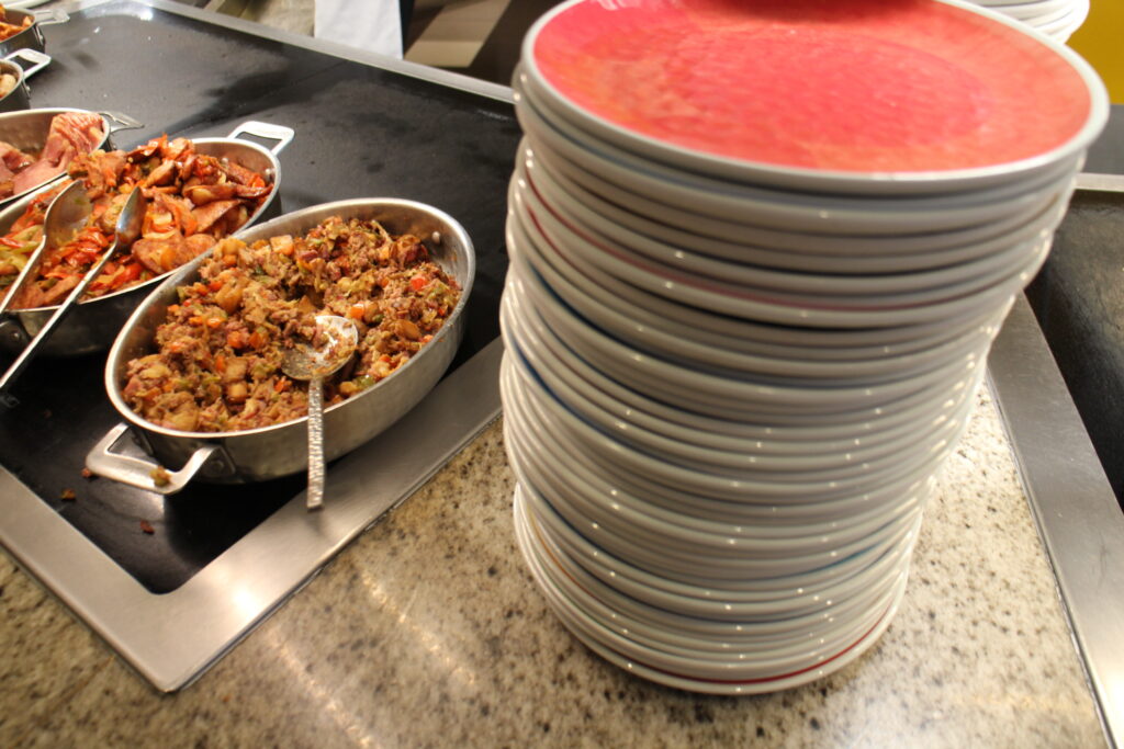 red stacked plates next to assorted meats on a buffet