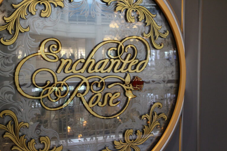 Entrance sign for Enchanted Rose bar and lounge at Disney with Enchanted Rose in gold cursive on a mirrored circle.