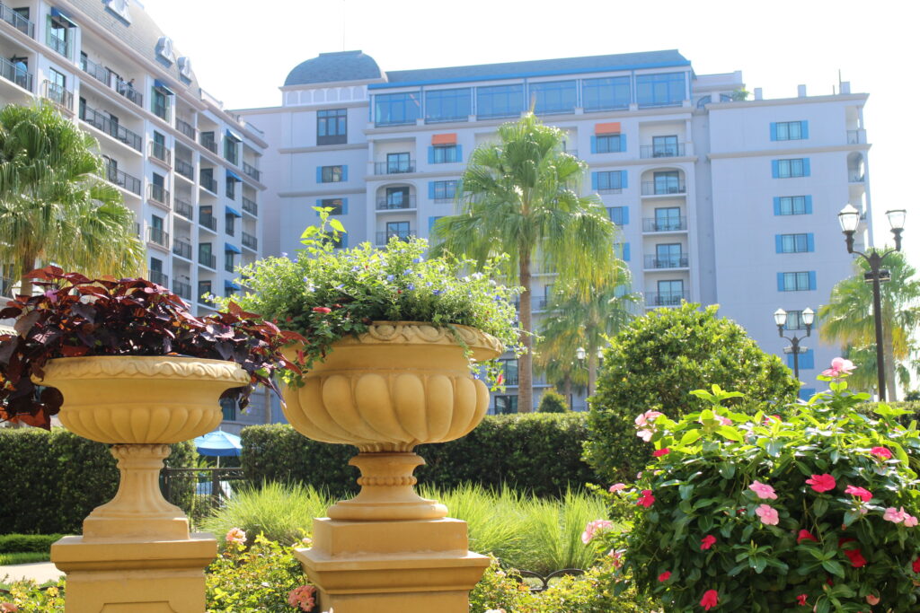 Flowers in decorative pots sit in front of the tall Riviera hotel building with Topolino's Terrace character meal at the top