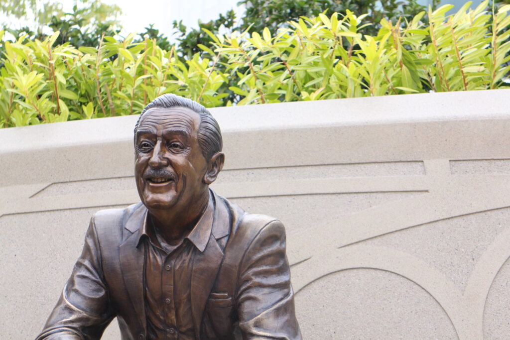 a bronze statue of Walt Disney sits on a step