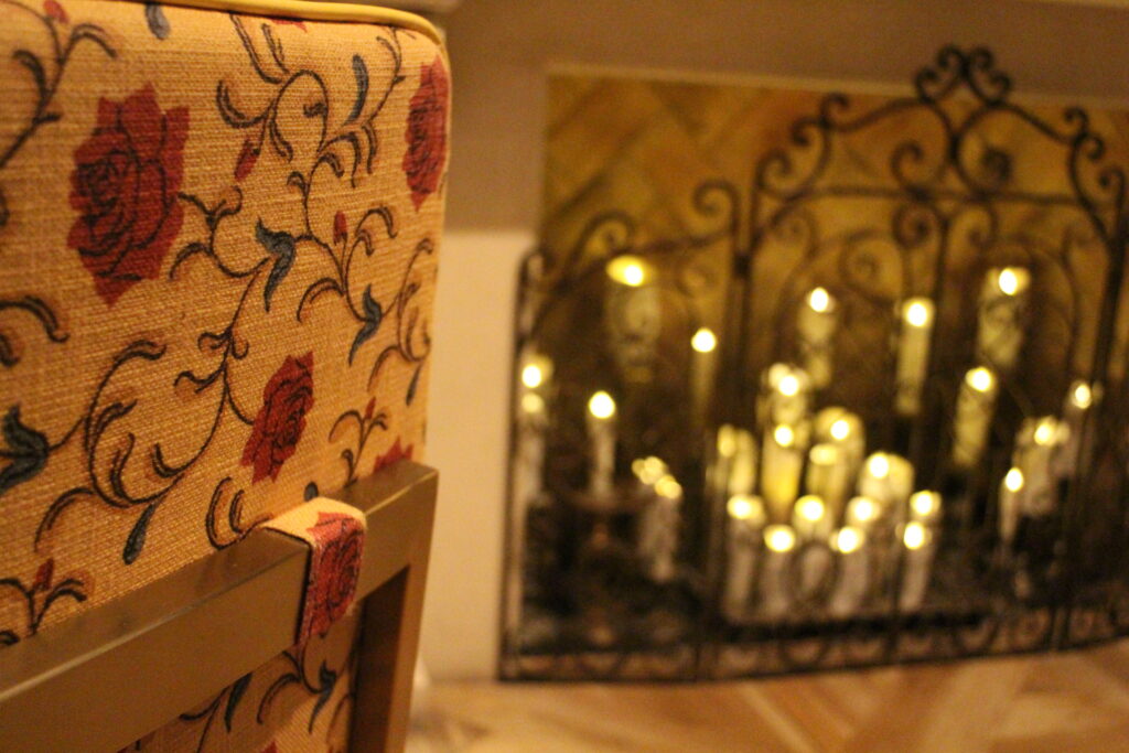 A yellow seat with a rose print sits in front of a fireplace lit by candles.