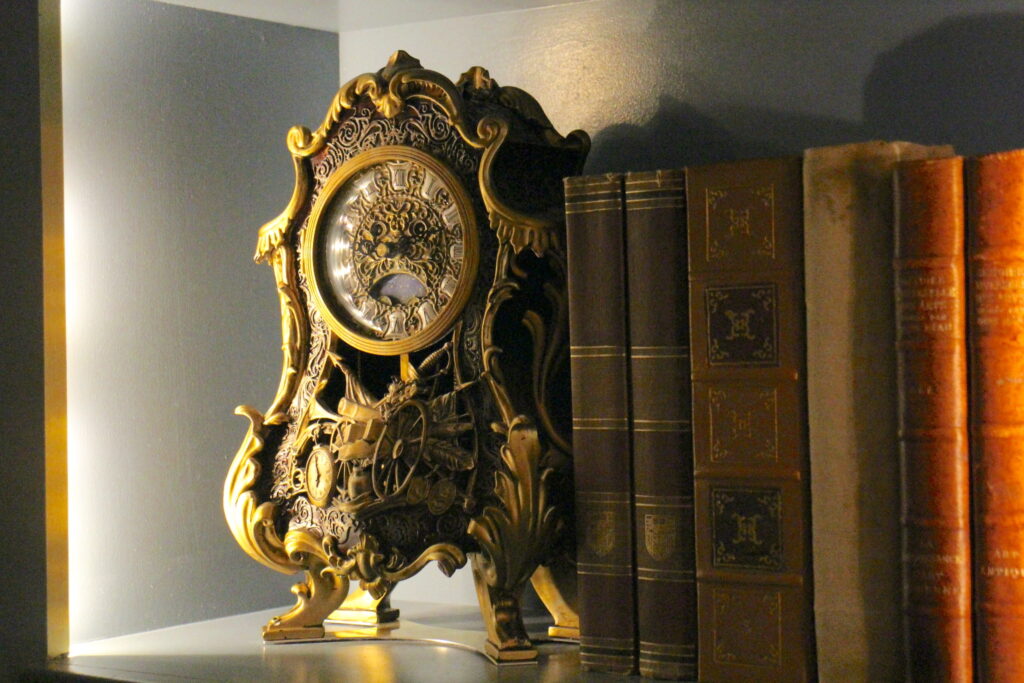 an ornate clock character sits on a bookshelf next to antique books