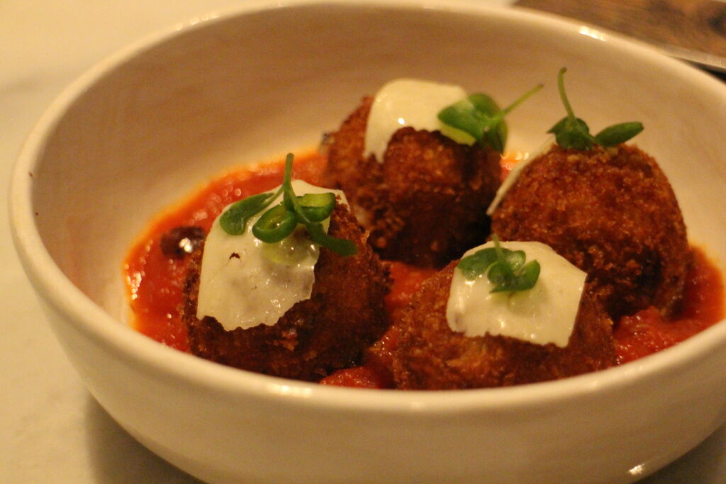 Enchanted Rose croquettes in a bowl with red sauce and topped with cheese and a green garnish.