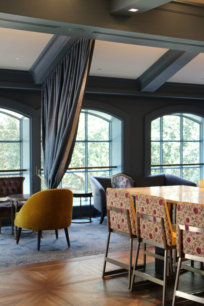 Inside one of the lounge rooms of Enchanted Rose, the tall windows line the walls, a hightop table has yellow chairs with a rose print on them.