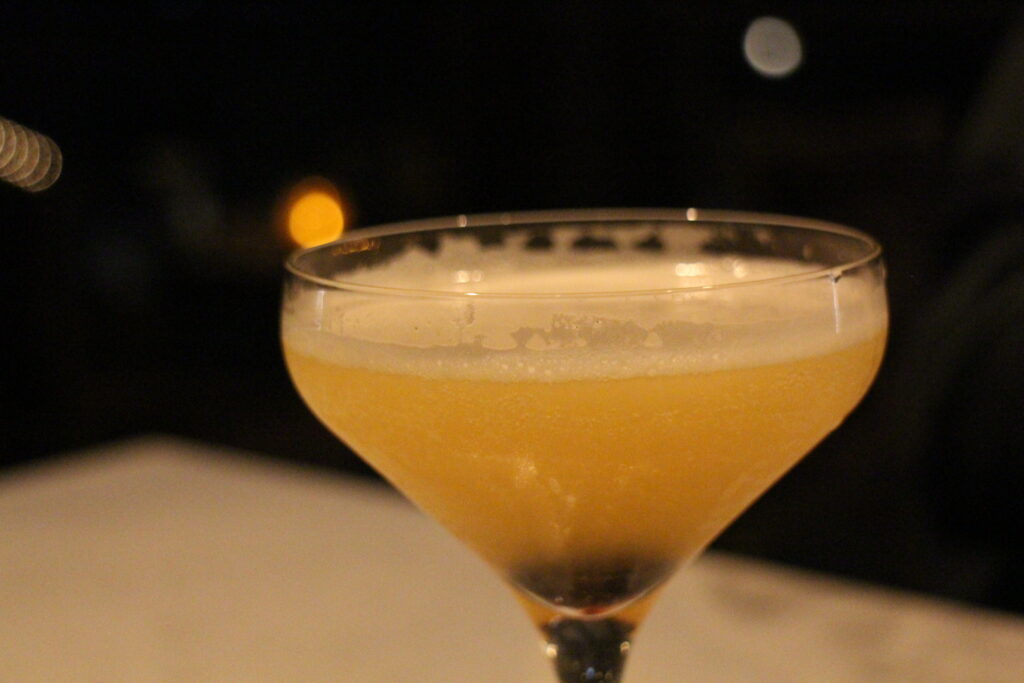 A golden cocktail in a glass sits on a gray table.