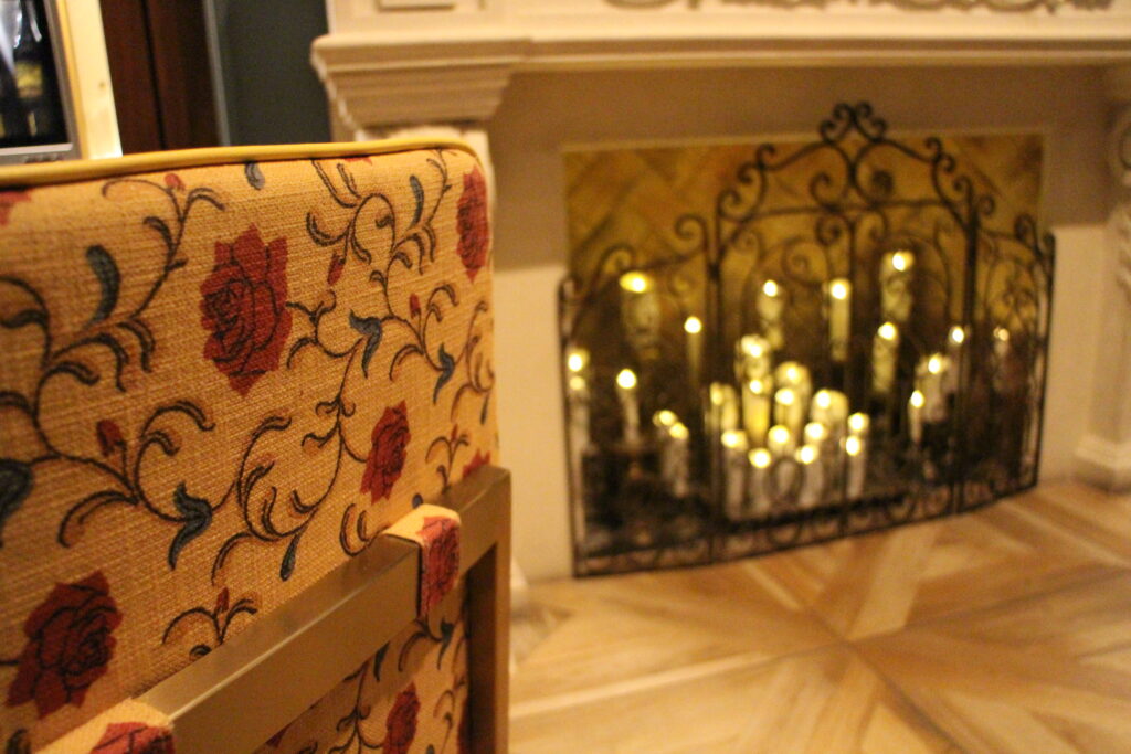 A yellow chair back with a rose print on it sits in front of a fireplace filled with candles at Enchanted Rose bar and lounge.