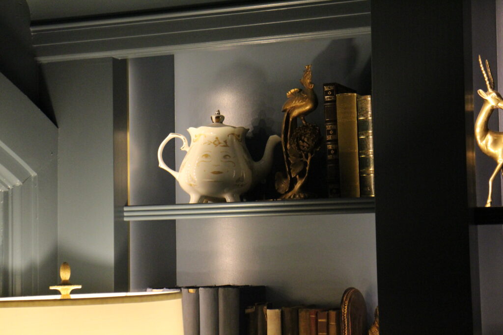 Mrs. Potts tea pot sitting on a dark bookshelf.