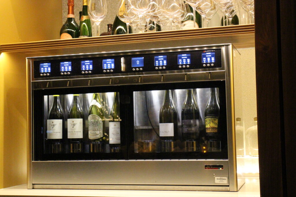 A refrigerated wine dispenser with multiple bottles in it and glasses on top.