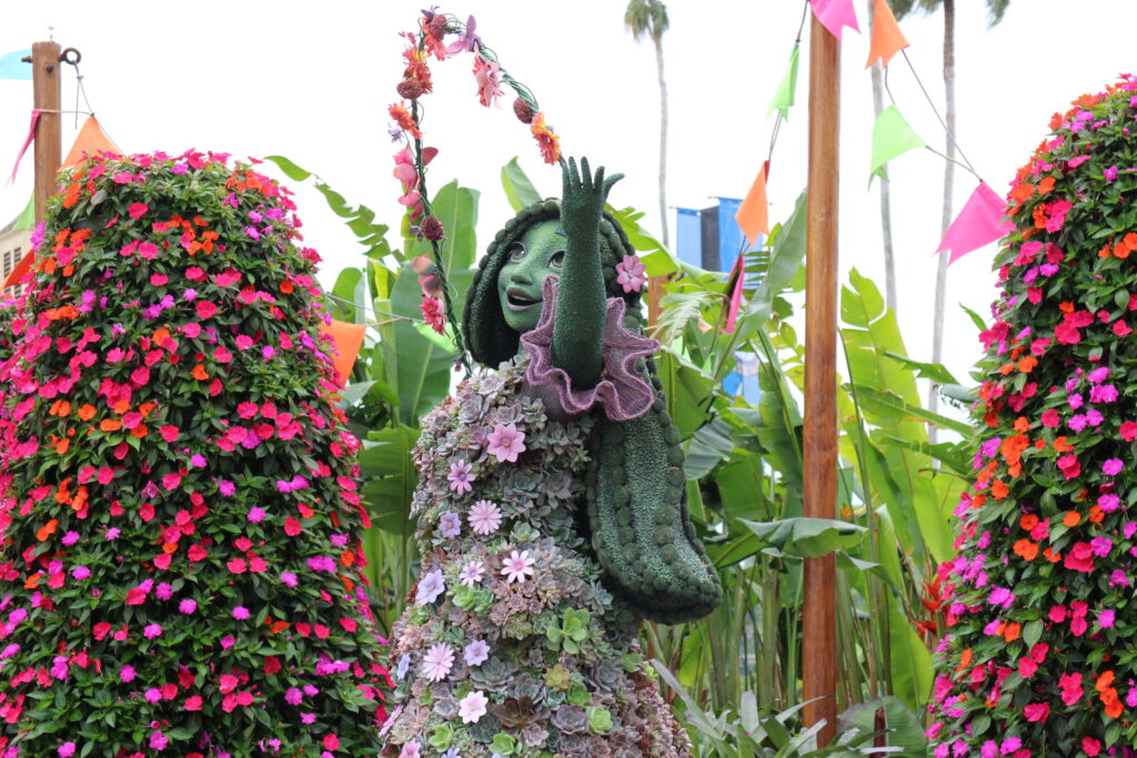 Isabela Madrigal from Encanto topiary at Epcot with a dress made of pastel succulents and surrounded by flower towers.