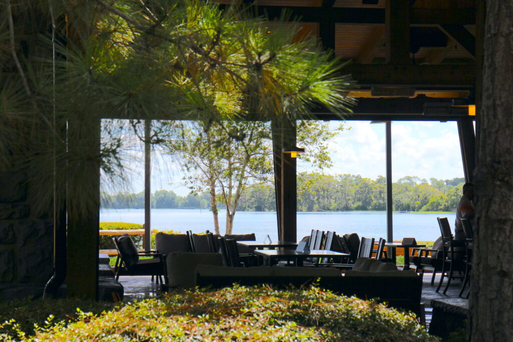 A look through a dark, silhouetted restaurant that reveals a beautiful lake view at Disney's Wilderness Lodhe, a DVC resort.