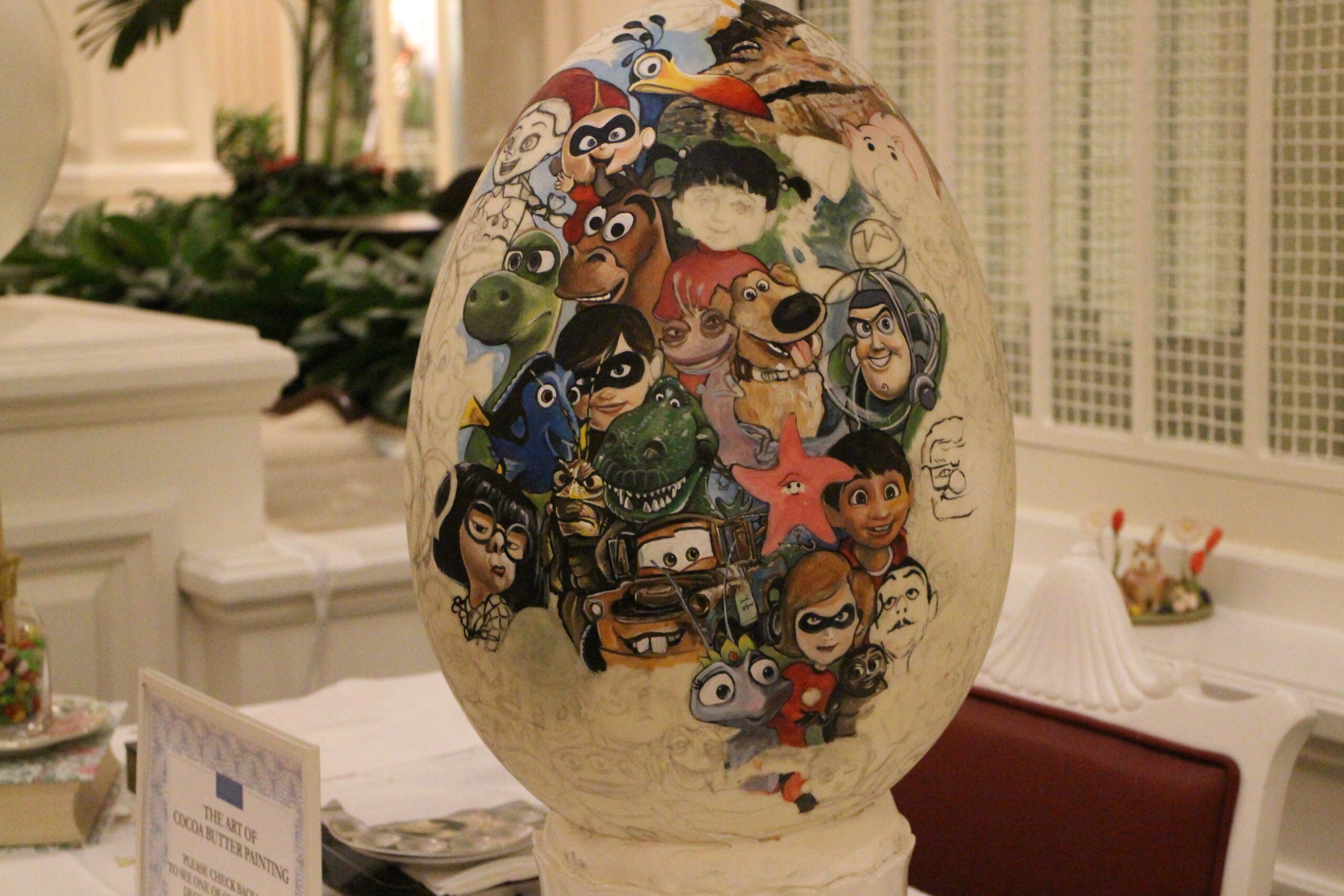 A large Easter egg sits on a table. It's off white with the faces of many Disney characters on it.