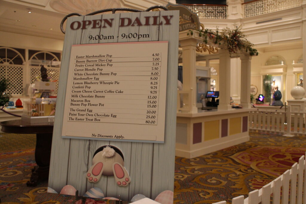A large menu sign with hours 9:00 a.m. to 9:00 p.m. and prices stands on an easel in front of the Grand Cottage structure.