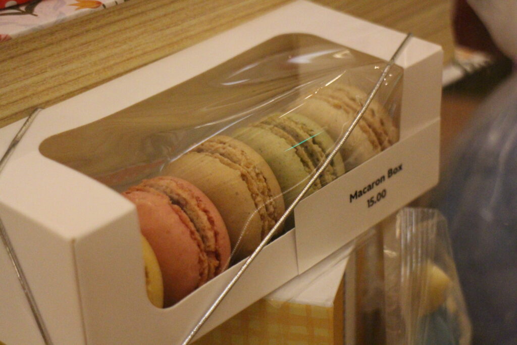 A white box with a clear top filled with colorful, pastel macarons.
