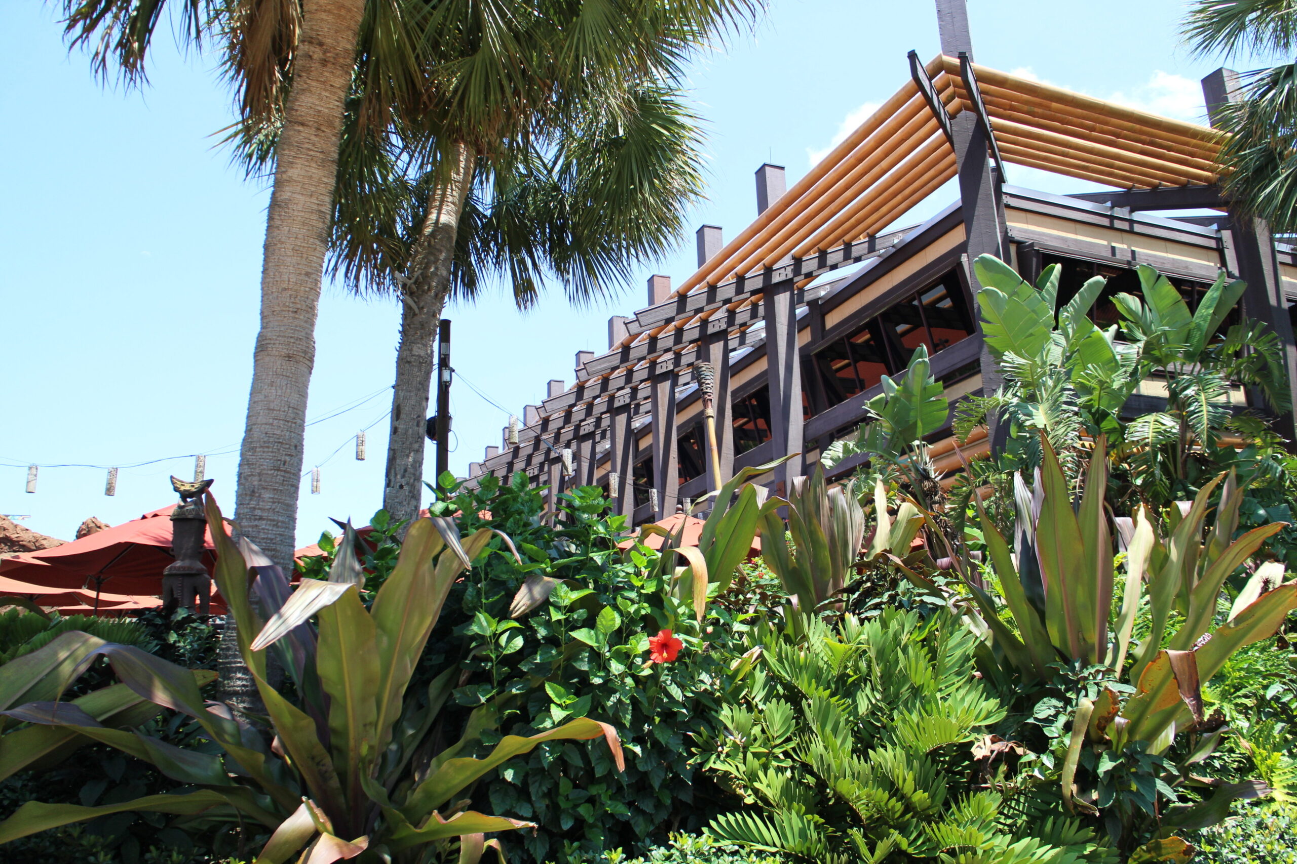 Polynesian resort tropical landscaping in front of a brown two story resort building with external support columns.