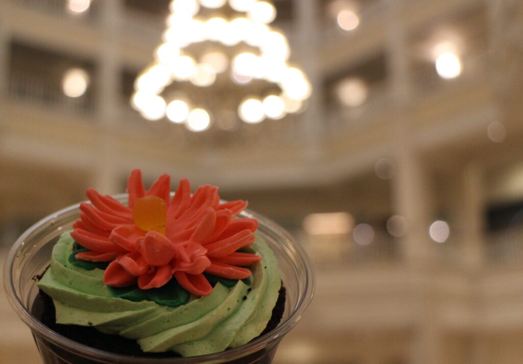 A pink flower cupcake treat at the Grand Floridian with the lobby chandelier out of focus in the background.