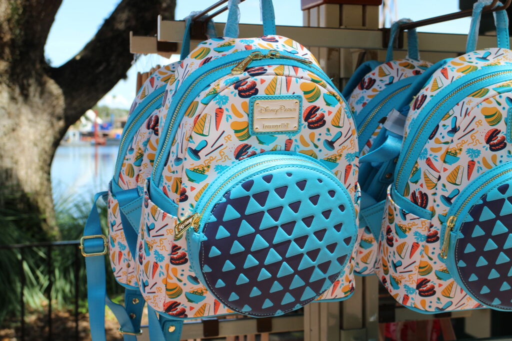 A colorful Epcot food festival backpack with Spaceship Earth on the front in blue and a food print on the main part of the backpack.